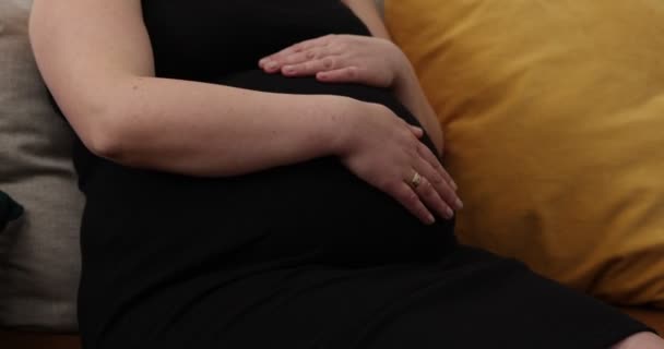 Šťastná těhotná žena se dotýká svého bříška doma. Těhotná žena odpočívající na pohovce, s bříškem — Stock video