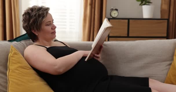 Šťastná těhotná běloška, která čte doma knihu. Těhotná žena odpočívající v ložnici — Stock video