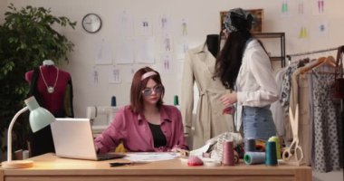 Moda tasarımcılarının ve terzilerin işi. Moda tasarımcıları stüdyolarında çalışıyor. Renkli Kumaşlar, Giysiler Asılma ve Dikiş Ögeleri Görünür