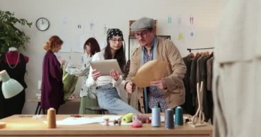 Moda tasarımcılarının ve terzilerin işi. Moda tasarımcıları stüdyolarında çalışıyor. Renkli Kumaşlar, Giysiler Asılma ve Dikiş Ögeleri Görünür.