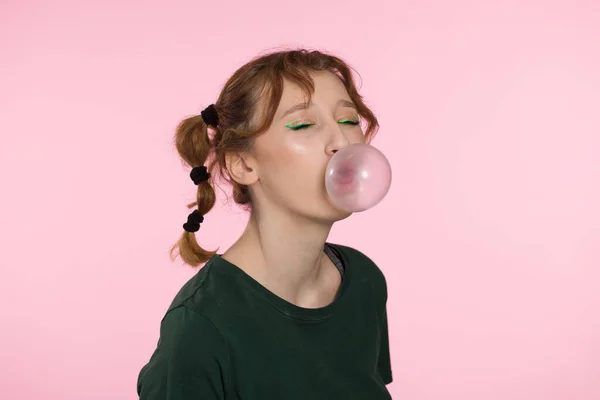 Bubble from chewing gum. Young teenage girl blowing pink bubble gum. Girl blowing large bubble isolated pink color background. — Stock Photo, Image