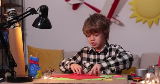 Kleiner Junge faltet Papierflugzeug und Schiffe, Kaukasus-Junge spielt mit Papierflugzeugen, zukünftiger Ingenieur-Designer, Hobby — Stockvideo