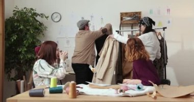 Moda tasarımcılarının ve terzilerin işi. Moda tasarımcıları stüdyolarında çalışıyor. Renkli Kumaşlar, Giysiler Asılma ve Dikiş Ögeleri Görünür.