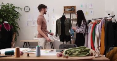 Moda tasarımcılarının ve terzilerin işi. Moda tasarımcıları stüdyolarında çalışıyor. Renkli Kumaşlar, Giysiler Asılma ve Dikiş Ögeleri Görünür.
