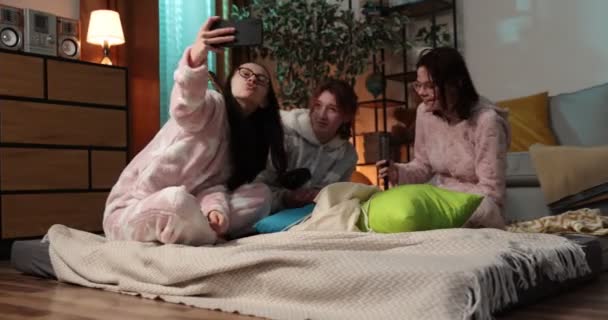 Vrouwelijke vrienden hebben plezier samen op het thuisfeest. Yonung vrouw in grappige onesies op pyjamafeest. — Stockvideo
