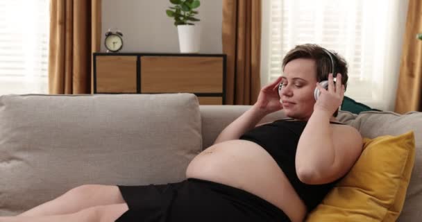 Mujer embarazada feliz escuchando música, quitándose los auriculares y sosteniendo cerca de la barriga — Vídeo de stock