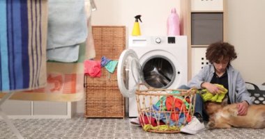 Ev işi. Çocuk evde çamaşır yıkıyor çamaşır makinesine çamaşır yüklüyor ve köpekle oynuyor..