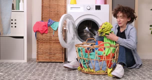洗脏衣服。衣服的味道很难闻。一个男孩厌恶地嗅着脏衣服，把它们扔进洗衣机 — 图库视频影像