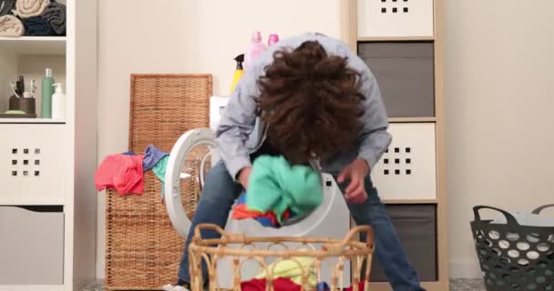 Gelukkig causasian tiener jongen gooien vuile kleren in de wasmachine als bal. Yong jongen hebben plezier gooien kleding in wasmachine in wasruimte. — Stockvideo