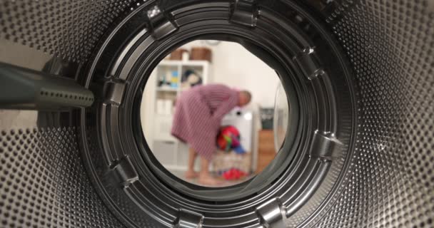 Uitzicht vanuit een wasmachine, een man zet een gekleurde was in de wasmachine — Stockvideo