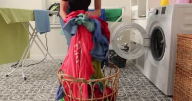 Kot pantolon ve gömlek giymiş gülümseyen genç bir çocuk bir çamaşır makinesinin önünde oturur. Kirli çamaşırları çamaşır makinesine yüklüyor. Parlak ve havadar bir çamaşır odası.