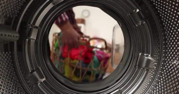 Вид зсередини пральної машини, чоловік кладе кольорове прання в пральну машину — стокове відео