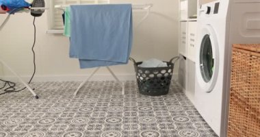 Kot pantolon ve gömlek giymiş gülümseyen genç bir çocuk bir çamaşır makinesinin önünde oturur. Kirli çamaşırları çamaşır makinesine yüklüyor. Parlak ve havadar bir çamaşır odası.