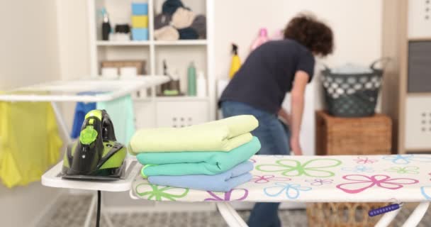 勤劳的青少年穿着蓝色衬衫，熨烫板上的熨斗，照顾衣服，在洗衣房做家务活 — 图库视频影像
