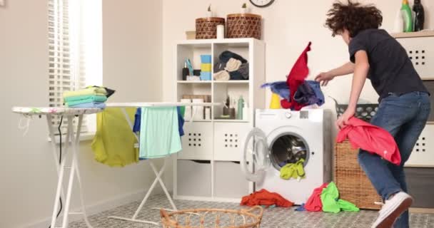 O rapaz está a brincar com roupas durante a lavandaria. Jovem adolescente jogando cesta com lavanderia — Vídeo de Stock