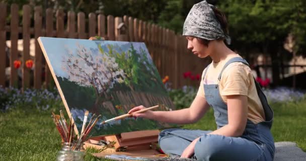 Uśmiechnięta dziewczyna maluje na płótnie akwarelami w ogrodzie — Wideo stockowe