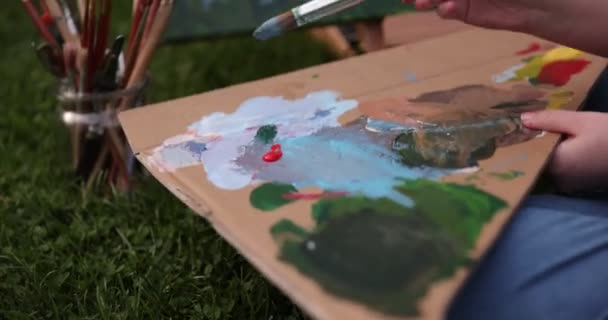 Uśmiechnięta dziewczyna maluje na płótnie akwarelami w ogrodzie — Wideo stockowe