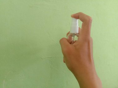 woman hand holding a white liquid soap dispenser on a green background.