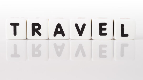 Travel spelled in dice letters reflected on white background.