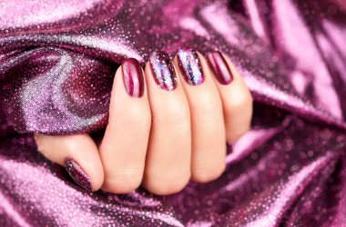 Parıltılı ve ışıltılı, şen mor manikürlü. Mor arka planda parlak mor manikürlü güzel bir kadın eli. Noel manikürü. Kapat..