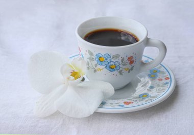 Kahve zamanı konsepti, bir fincan kahve ve beyaz kumaşlı güzel beyaz orkide, açık hava çekimi.