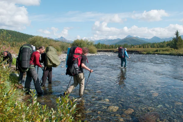 Randonneurs traversant la rivière de montagne, Oural, Russie Image En Vente