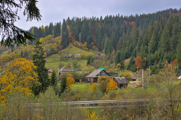 A small village located in a mountain valley. Autumn mountain landscape in the Ukrainian Carpathians - yellow and red trees combined with green needles. Panoramic view.