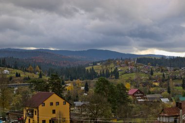 Bir dağ vadisinde küçük bir köy. Ukrayna Karpatları 'ndaki sonbahar dağ manzarası. Sarı ve kırmızı ağaçlar yeşil iğnelerle birleşmiş. Panoramik görünüm.
