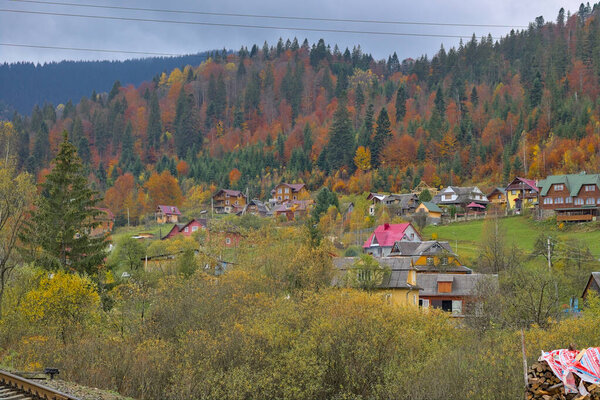 A small village located in a mountain valley. Autumn mountain landscape in the Ukrainian Carpathians - yellow and red trees combined with green needles. Panoramic view.