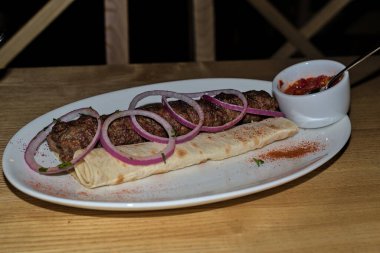 Traditional Georgian national cuisine. Lula kebab from minced meat (beef, lamb, veal) on pita bread (lavash). With red onions. Portion luleh kebab on a plate.
