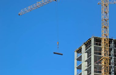 Yüksek katlı bir konut kompleksinin modern yapısının soyut bir parçası. Gökyüzünde bir vinç, kurulum için büyük ölçekli bir ürünü hareket ettirir. Mavi gökyüzü.