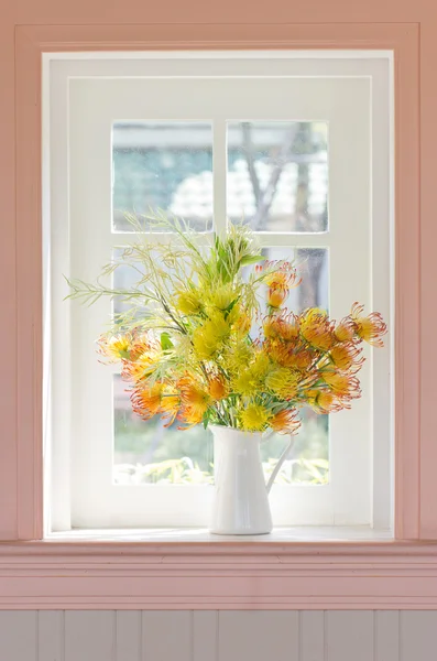 Fleurs artificielles en vase blanc à côté de la fenêtre blanche . — Photo