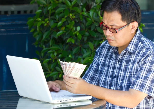 Hombre asiático con portátil y su billete tailandés . —  Fotos de Stock