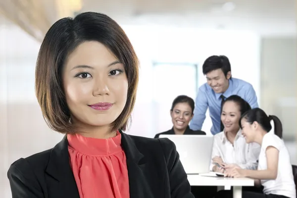 Beautiful Chinese Business woman with colleagues working behind.