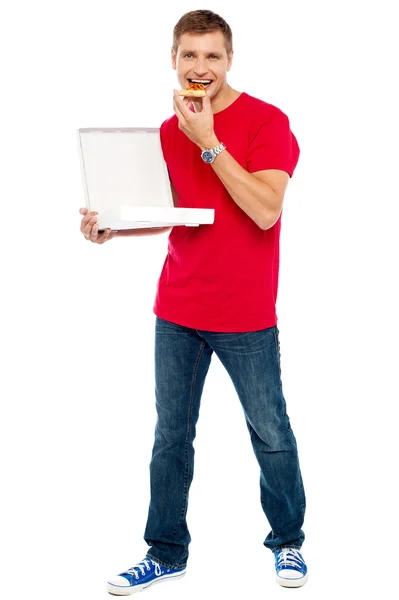 Причинно умный парень держит коробку пиццы и ест кусок — стоковое фото
