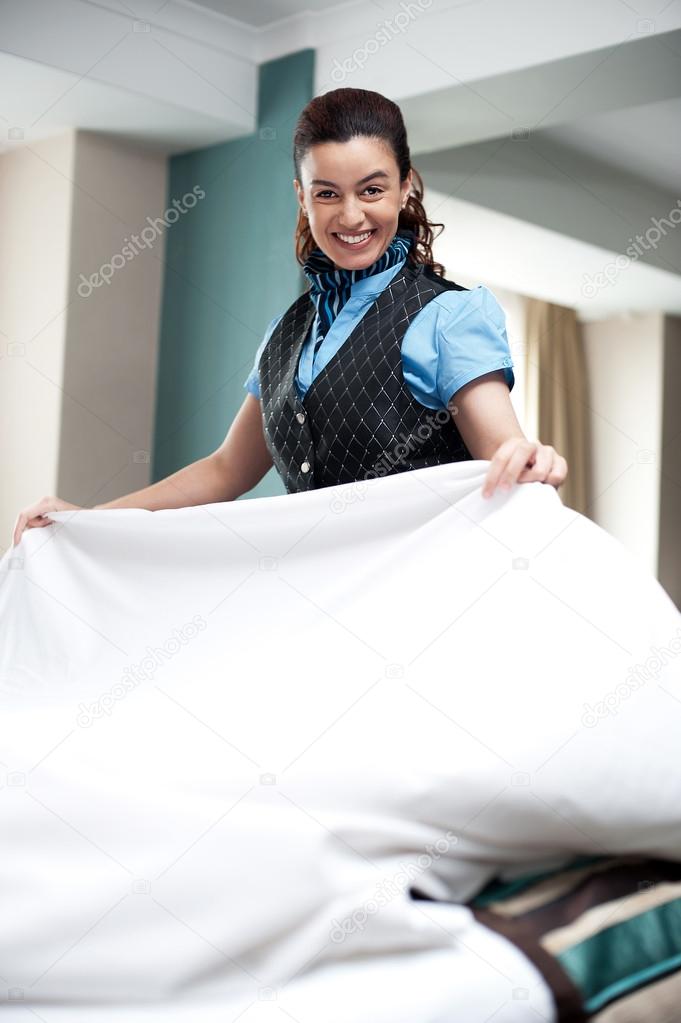 Enthusiastic female attendant arranging bed sheet