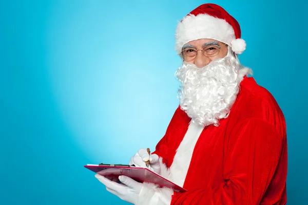 Een grondig moderne santa claus controleert zijn lijst op Klembord — Stockfoto