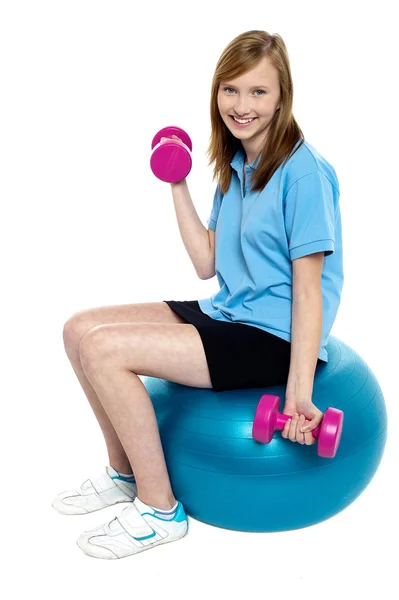 Jolie adolescente assise sur une boule de pilate bleue faisant des haltères — Photo