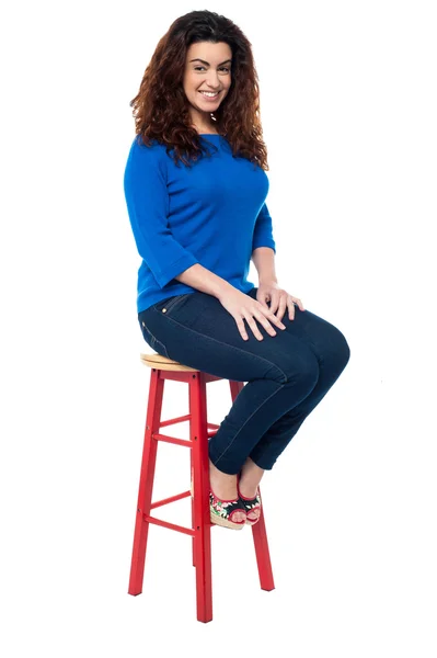 Long curly haired lady seated on red stool — Stock Photo, Image