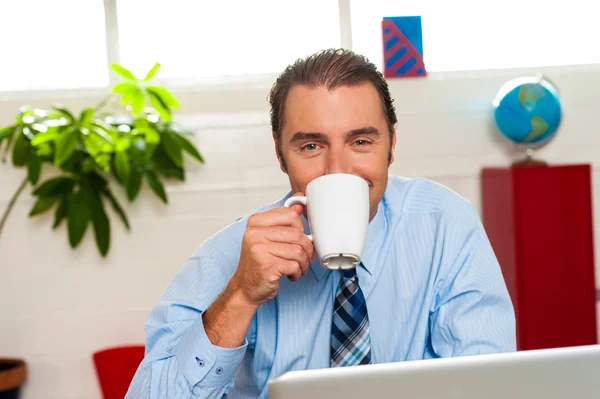 Улыбающийся мужчина-менеджер наслаждается горячим кофе — стоковое фото