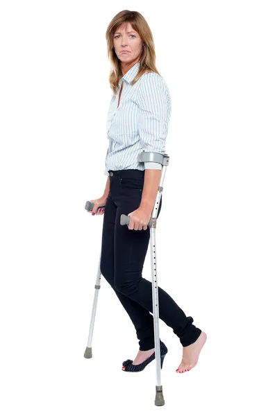 Pensive looking woman using crutches to walk — Stock Photo, Image