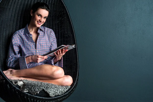 Улыбающаяся женщина на пузырьковом кресле читает журнал — стоковое фото