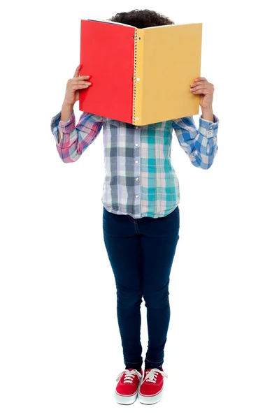 Escola menina escondendo seu rosto com um livro — Fotografia de Stock