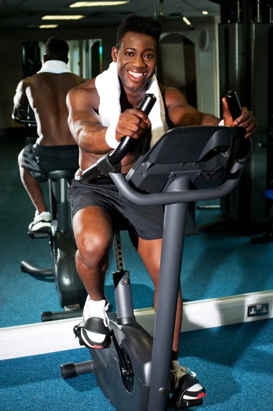 Homem musculoso em bicicleta excercise no ginásio — Fotografia de Stock