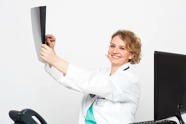 Smiling doctor looking at scanned x-ray report — Stock Photo, Image