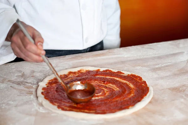 Koch Bäcker verteilt Sauce auf Pizzaboden — Stockfoto