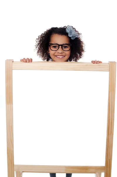 Chica espiando desde detrás del tablero de escritura blanco — Foto de Stock