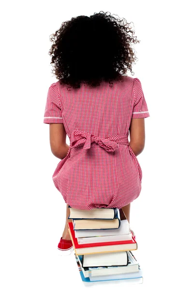 Meisje, zittend op stapel boeken geconfronteerd met de muur — Stockfoto