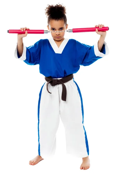 Mladá dívka v karate uniformě, drží nunchucks执行堆栈的书籍的活动学校子 — Stock fotografie