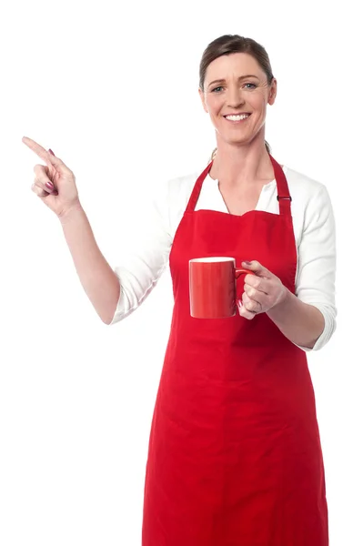Радостная женщина с кофейной кружкой, указывающей в сторону — стоковое фото
